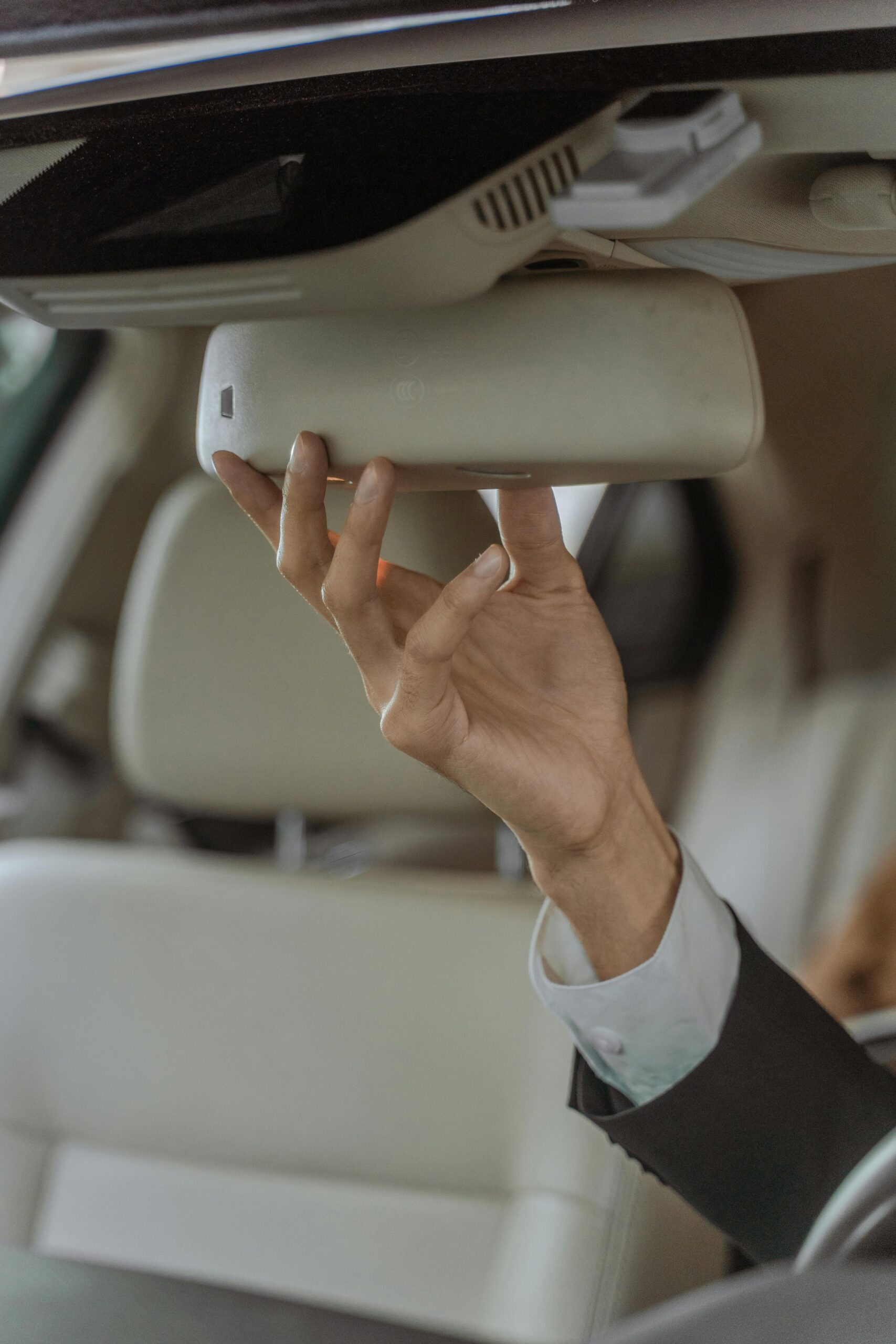 A professional chauffeur in a suit adjusting the rear-view mirror in an elegant car interior, focusing on precision and safety.